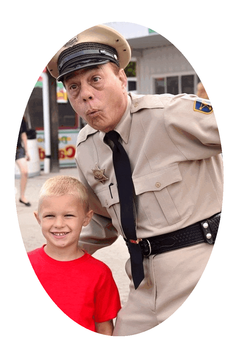 Picture of a boy standing next to an amusement park character employee who is wearing a costume that resembles fictional deputy sheriff Barney Fife.