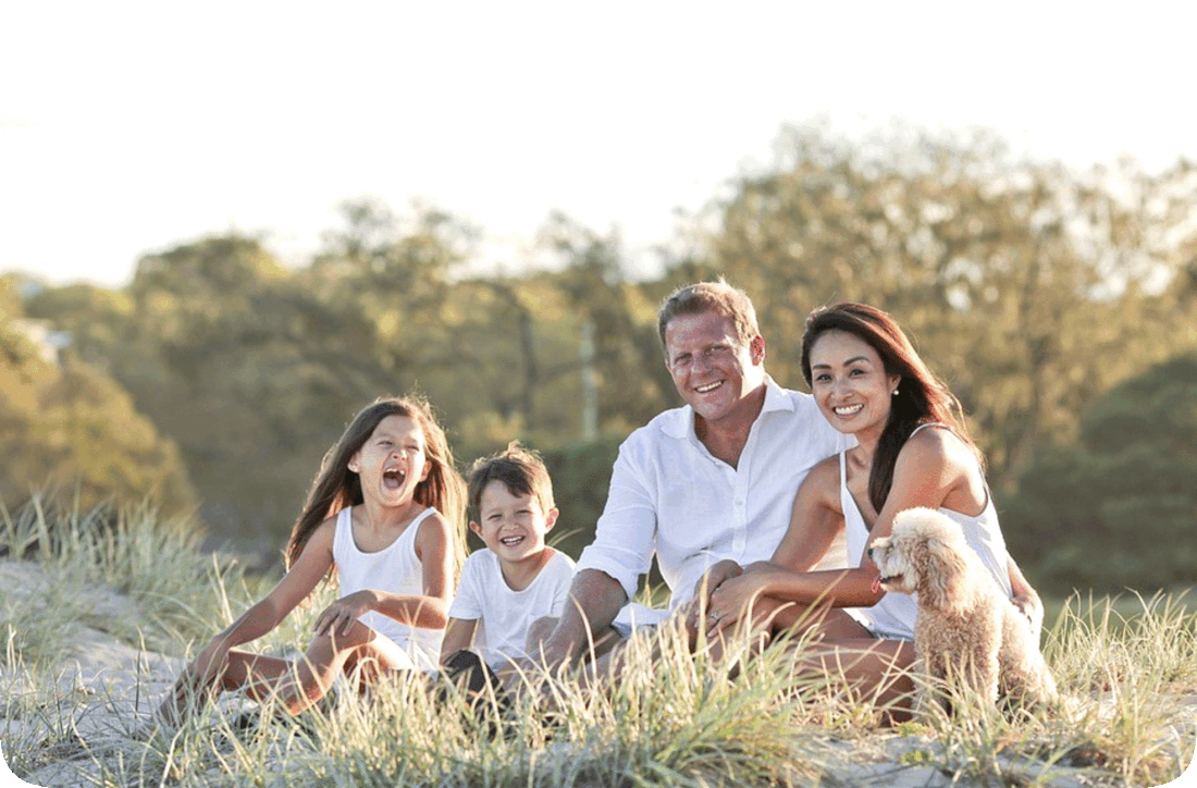 Picture of a happy smiling family outdoors in a grassy area with trees in the background.