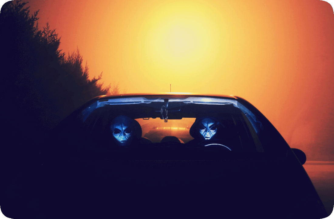 Picture of two space aliens in an automobile, one as the driver and the other as the passenger, driving along a dark road.
