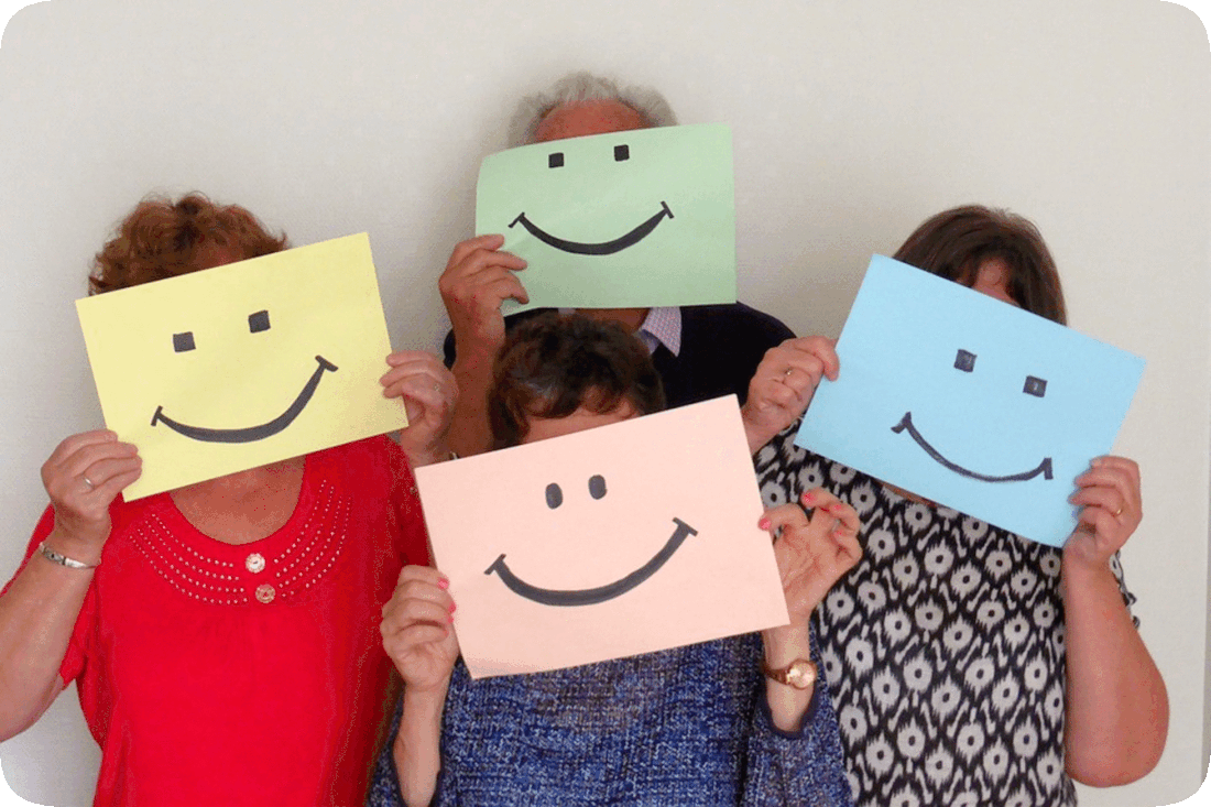 Picture of four people holding up smiley faces printed on colored paper.