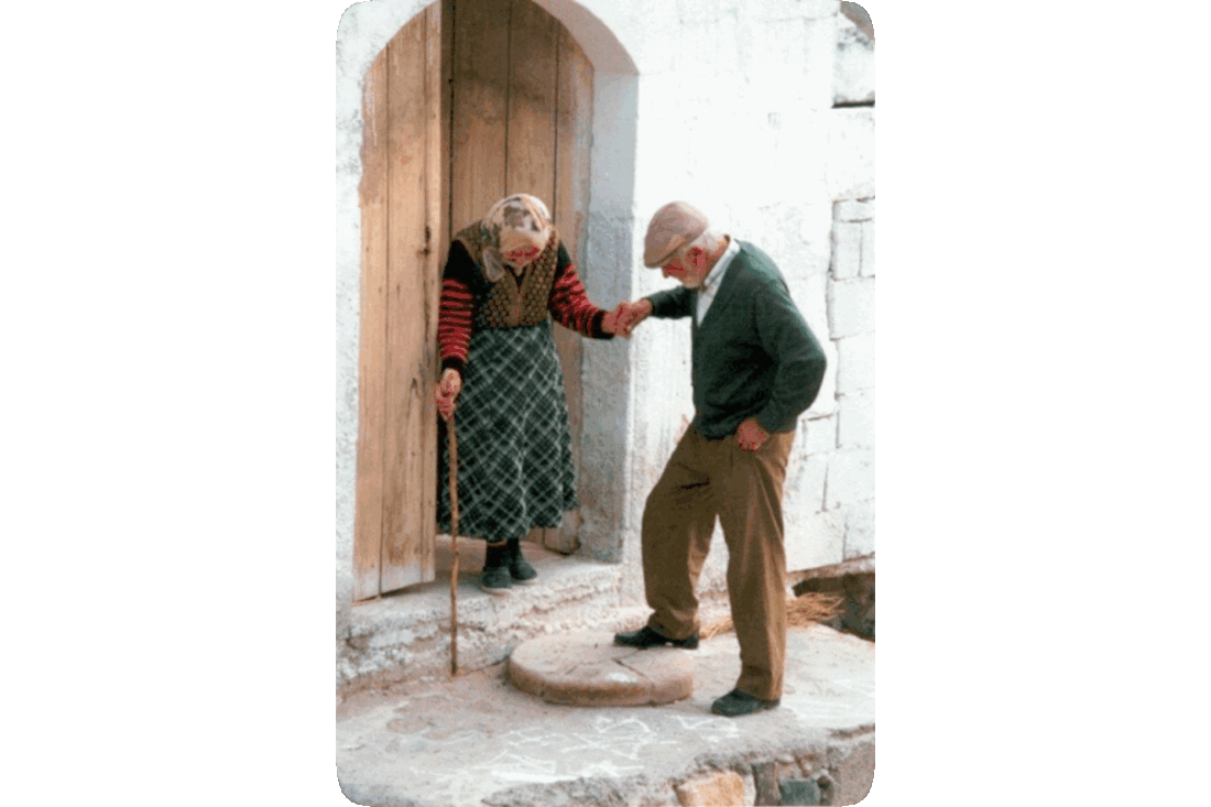 Picture of a man holding an elderly woman’s hand to support her as she crosses a doorstep and goes down one step.