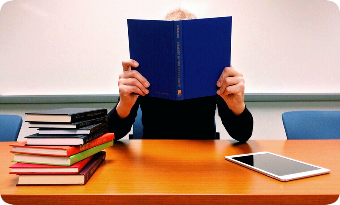 Picture of a student holding up an open book to hide behind.