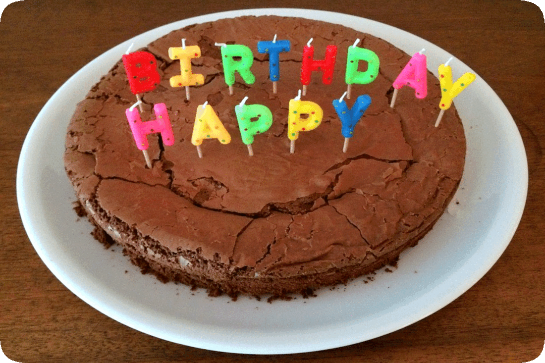 Picture of a plain cake with no frosting on a dinner plate and unlit letter-shaped candles reading, Birthday Happy’ placed somewhat haphazardly on the cake.