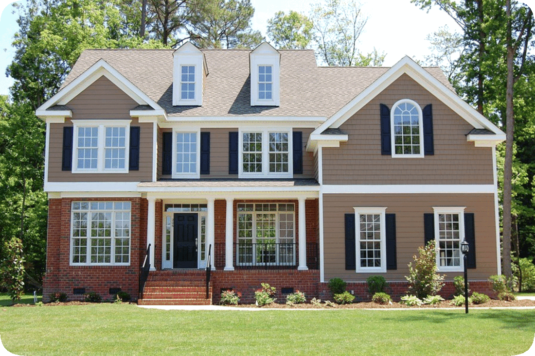 Picture of a two-story single-family house with a green lawn, flowering plants, and green leafy trees around it.