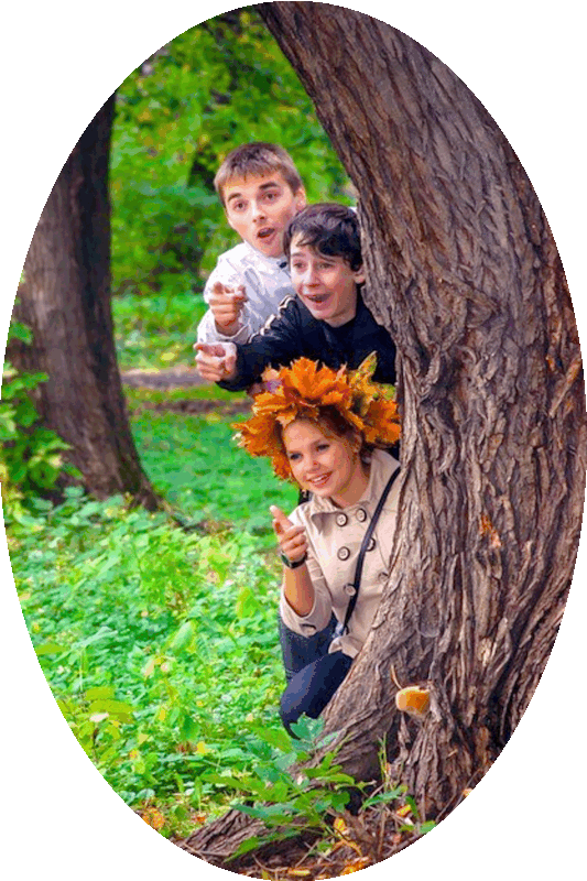 Picture of three happy smiling people peering out from behind a tree trunk.