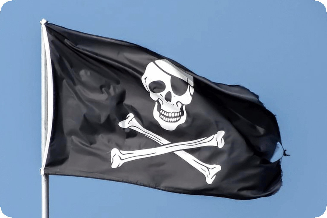 Picture of a pirate flag with a skull and crossbones on it flying from a flagpole and a clear blue sky in the background.