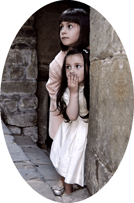 Picture of two girls peering out from the recessed doorway of an old stone building.