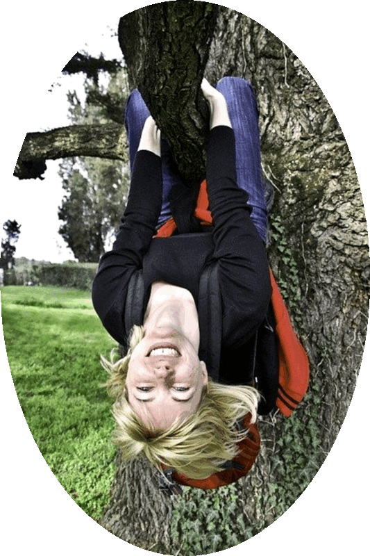 Picture of a happy smiling woman hanging upside down by her arms and legs from a tree branch.