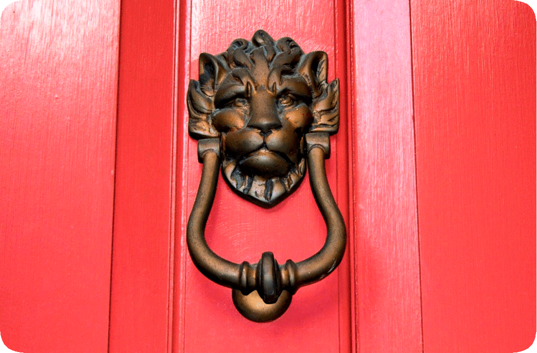 Picture of a red door with brass door knocker that has a lion’s face image on it.