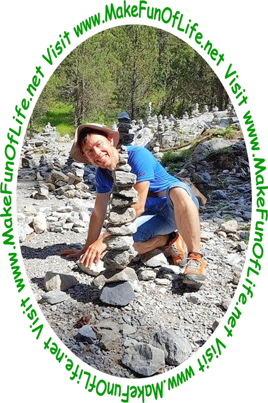 Picture of a happy smiling man stacking stones one on top of another, in a wilderness area with tall dark green evergreen trees.