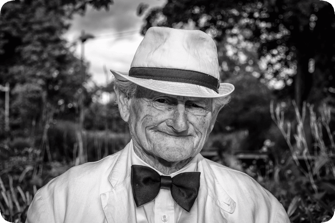 Picture of a man standing outside and wearing a hat, bowtie, and jacket.