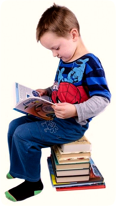 Picture of a boy sitting on a stack of books and reading a book.