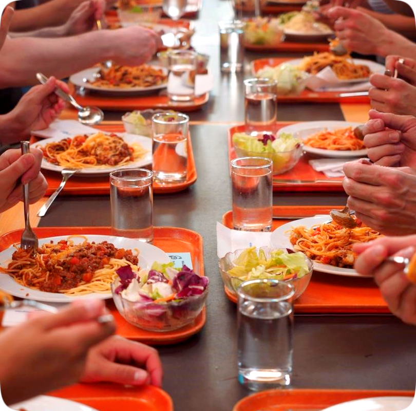 Picture of people at a long table eating a meal of spaghetti, salad, and water