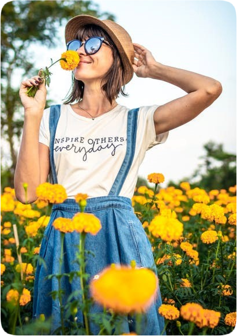 Picture of a happy smiling woman standing in a field of bright yellow flowers, wearing a t-shirt with the words, 'Inspire others every day.'