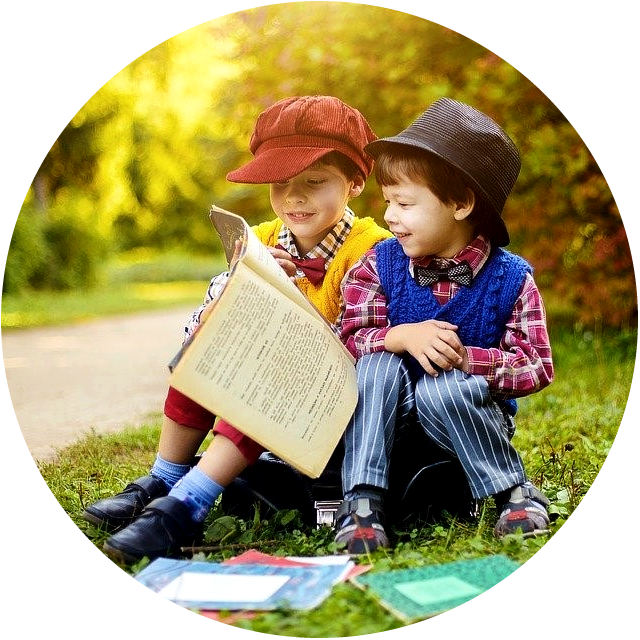 Picture of two happy smiling boys sitting in a grassy area and looking at a book.
