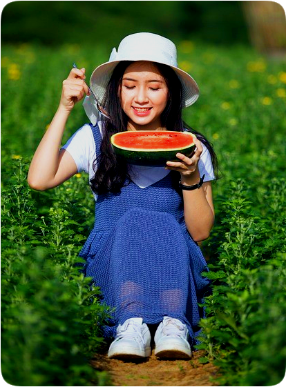 Picture of a happy smiling woman sitting in a field and eating watermelon.