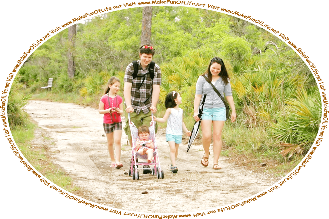 Picture of a family of 5, with a husband, wife, and 3 daughters, strolling through a park on a sandy trail, with green grass and semi-tropical green leafy plants and trees on both sides of the trail, and the words, ‘Visit www.MakeFunOfLife.net.’