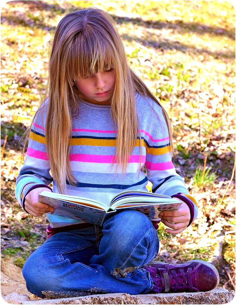 Picture of a girl sitting on the ground outdoors and reading a book.