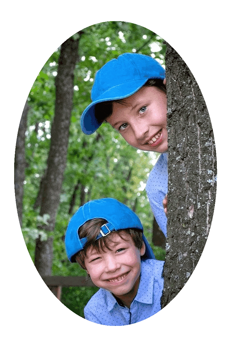 Picture of two happy smiling boys peering out from behind a tree.