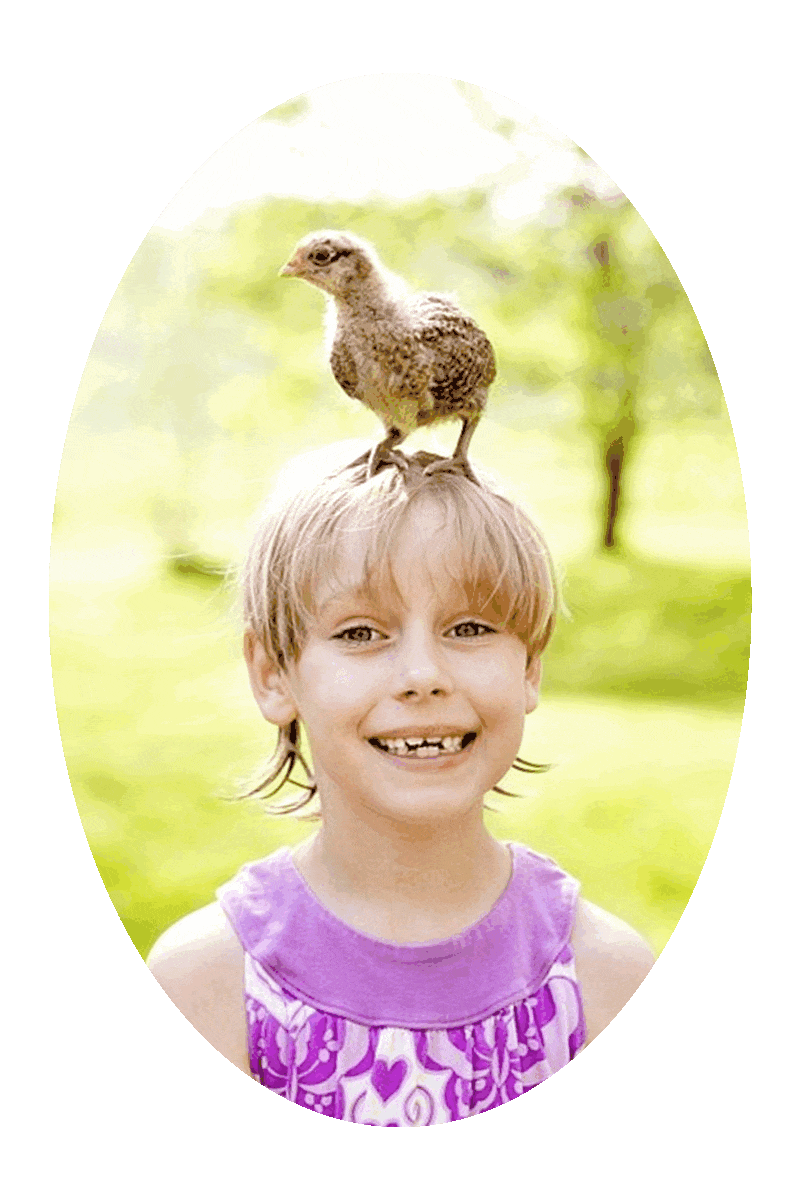 Picture of a happy smiling girl with a bird standing on top of her head.