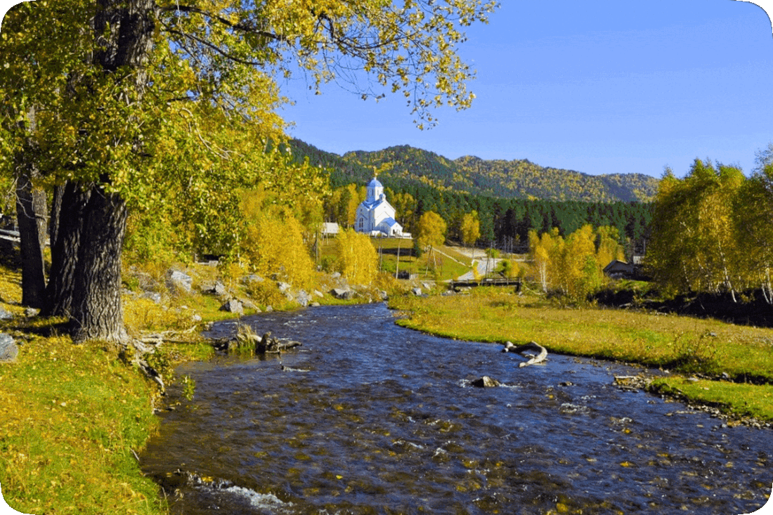 Picture of a church in a wilderness area, with green grass, green tree-covered hills and mountains, and a shallow brook running below the church.