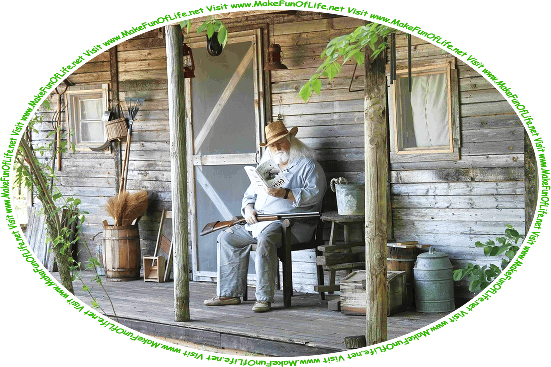 Picture of a man with a beard and shoulder-length white hair sitting on a chair on the porch of a small rustic wooden house in a woods, reading a book, with a double-barreled shotgun resting across his lap, and the words, ‘Visit www.MakeFunOfLife.net.’