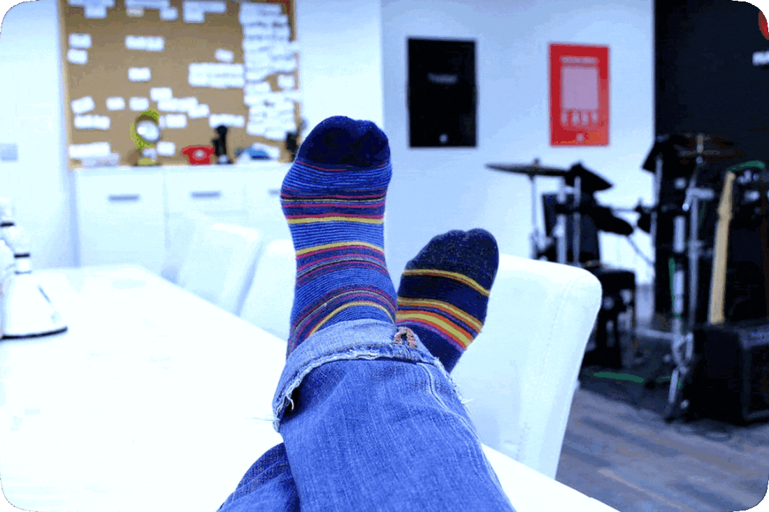 Picture of a person’s feet propped up on a table, while wearing dark blue socks with thin red, yellow, and light blue stripes.