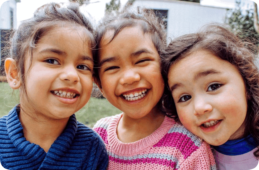 Picture of three happy smiling girls standing outside in a grassy area with houses in the background.