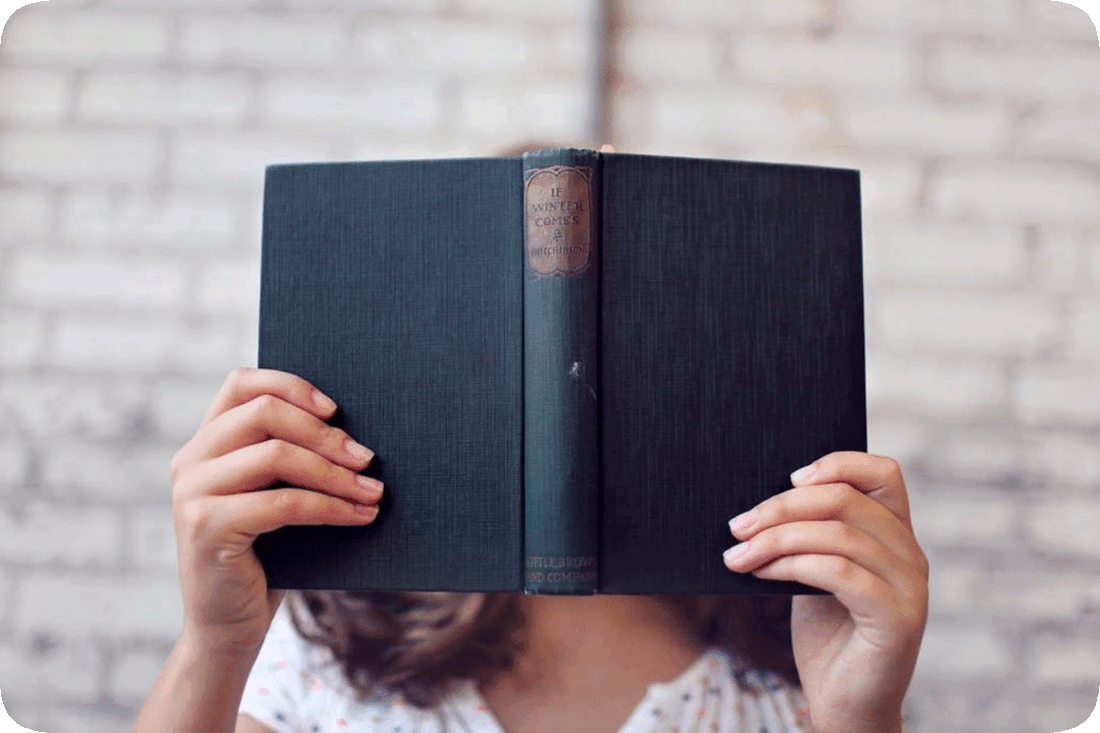 Picture of a woman reading a book that she is holding up in front of her face.