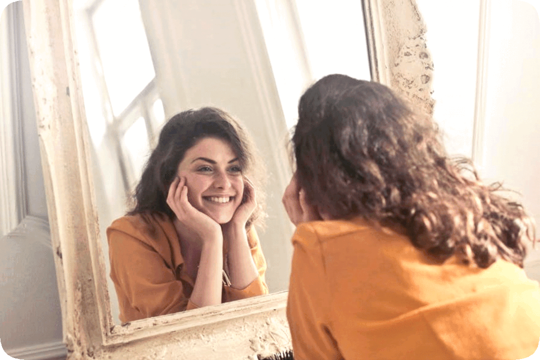 Picture of a happy smiling woman looking at herself in a mirror.