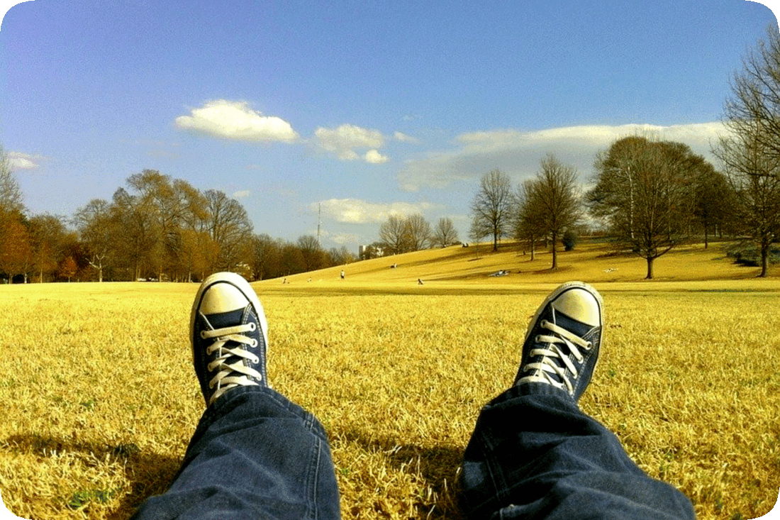 Picture of the feet of a person who is lying down on the grass in a park.