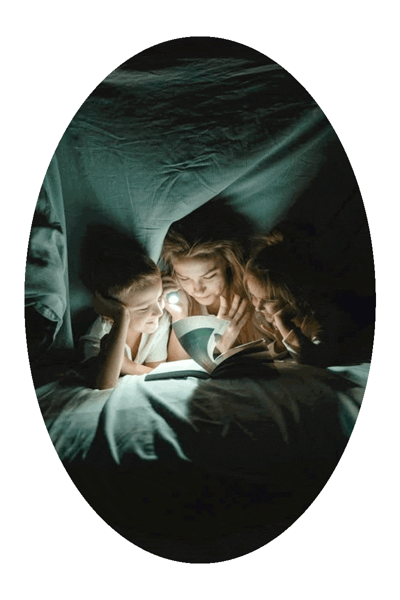 Picture of a woman using a flashlight in the dark to read a book to two children.