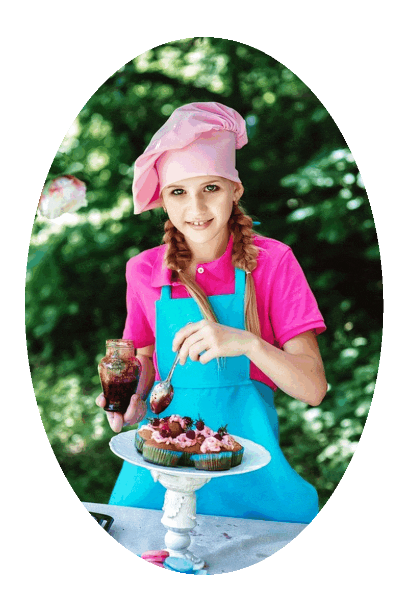 Picture of a young lady standing at a table under a tree and spooning toppings onto cupcakes.