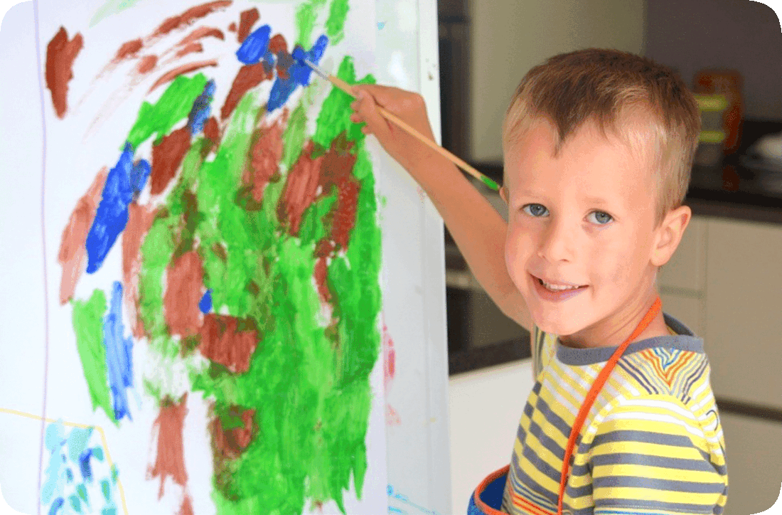 Picture of a happy smiling boy holding a paintbrush over an abstract painting he is making.