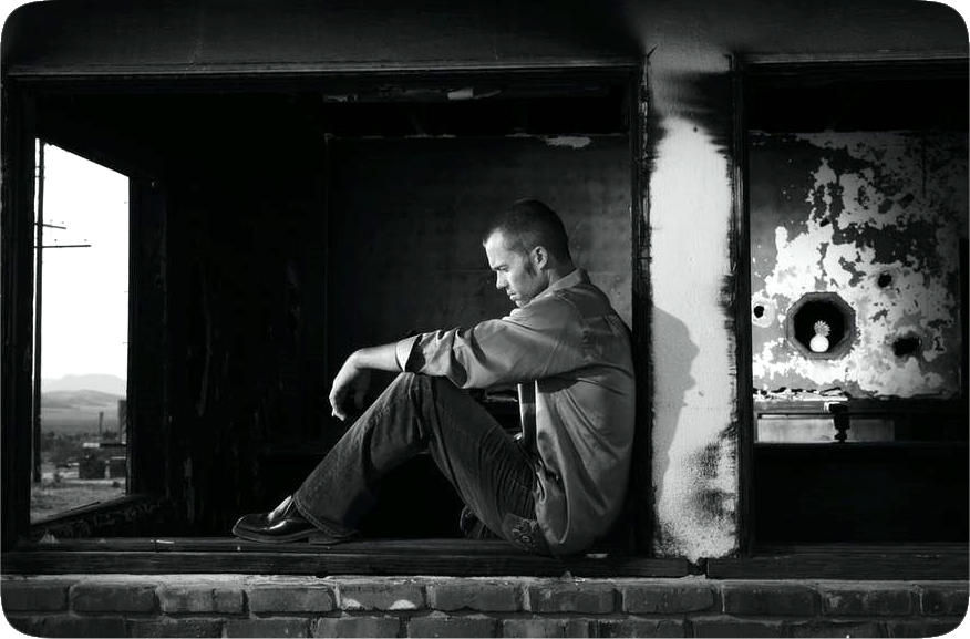 Picture of a downcast looking man sitting in a partially-burned-out building.